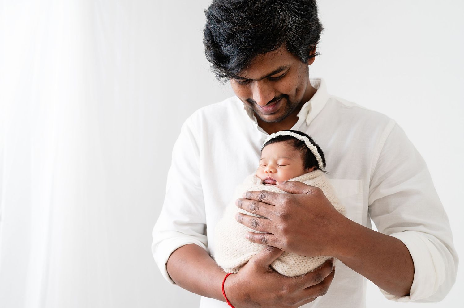 Parent in white shirt tenderly holding swaddled newborn against bright background.