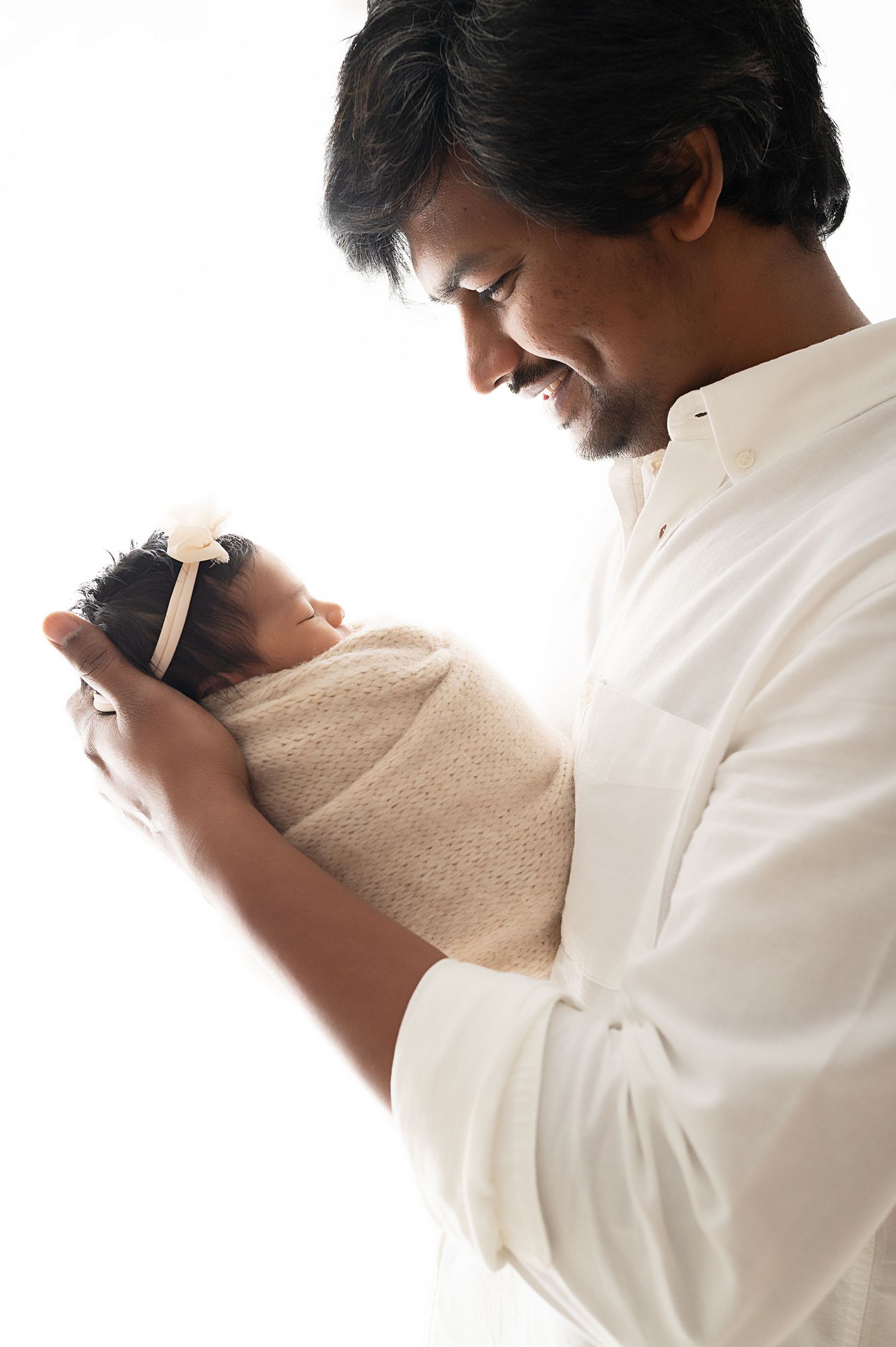 Parent gazing lovingly at swaddled newborn in gentle studio portrait against white background.
