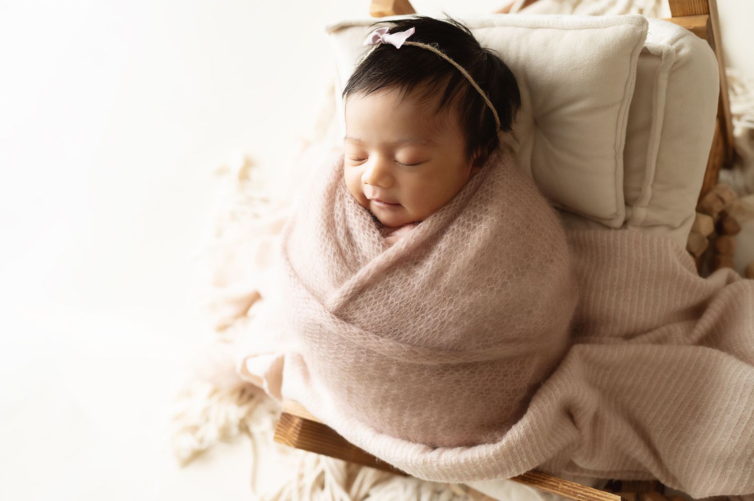 Sleeping baby wrapped in soft pink blanket resting on textured cushion.
