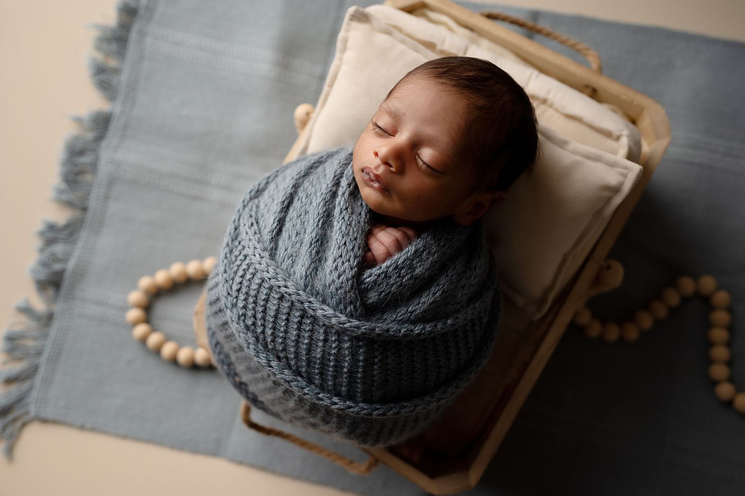 A sleeping newborn wearing a gray knit hat rests on wooden prop during photo session.