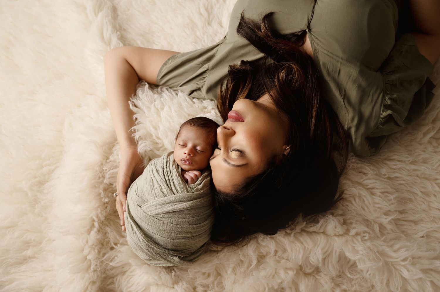 A sleeping newborn and person lay together on white bedding during lifestyle photo session.