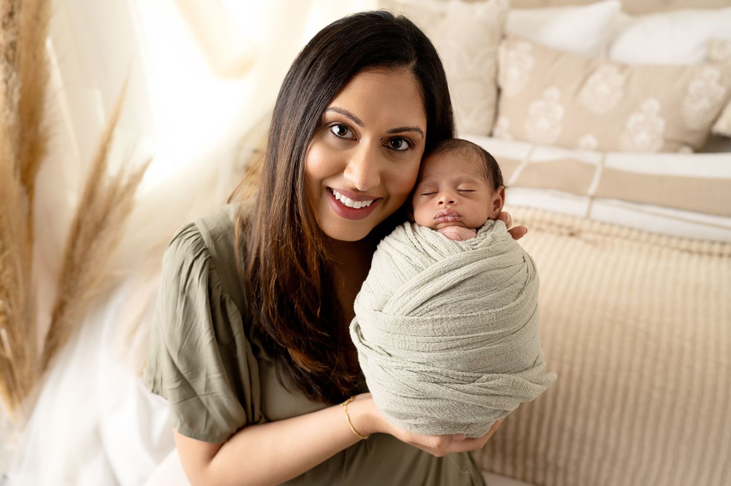 A person holds a sleeping newborn wrapped in soft gray swaddling fabric.