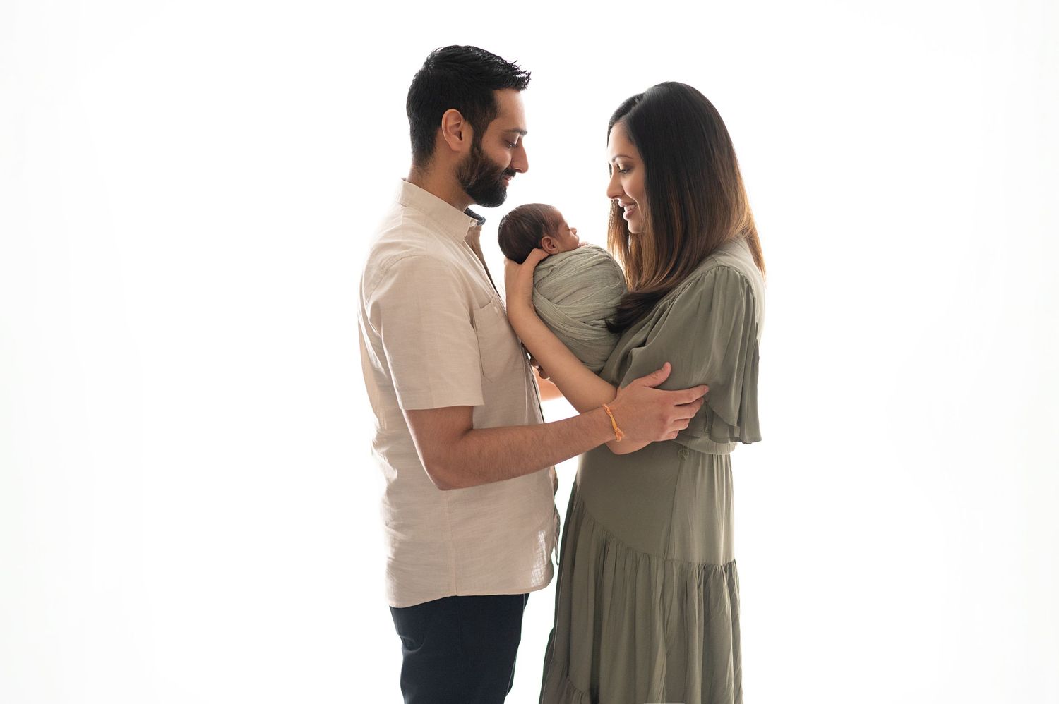 A couple holds their newborn baby together in a tender embrace against white backdrop.