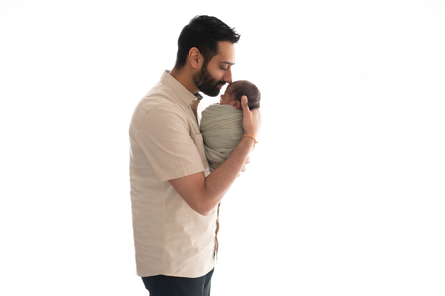 A person gently cradles a newborn baby wrapped in soft fabric against their chest.