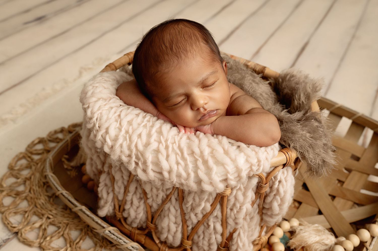 Newborn baby sleeping in textured cream basket with cozy knitted blanket.