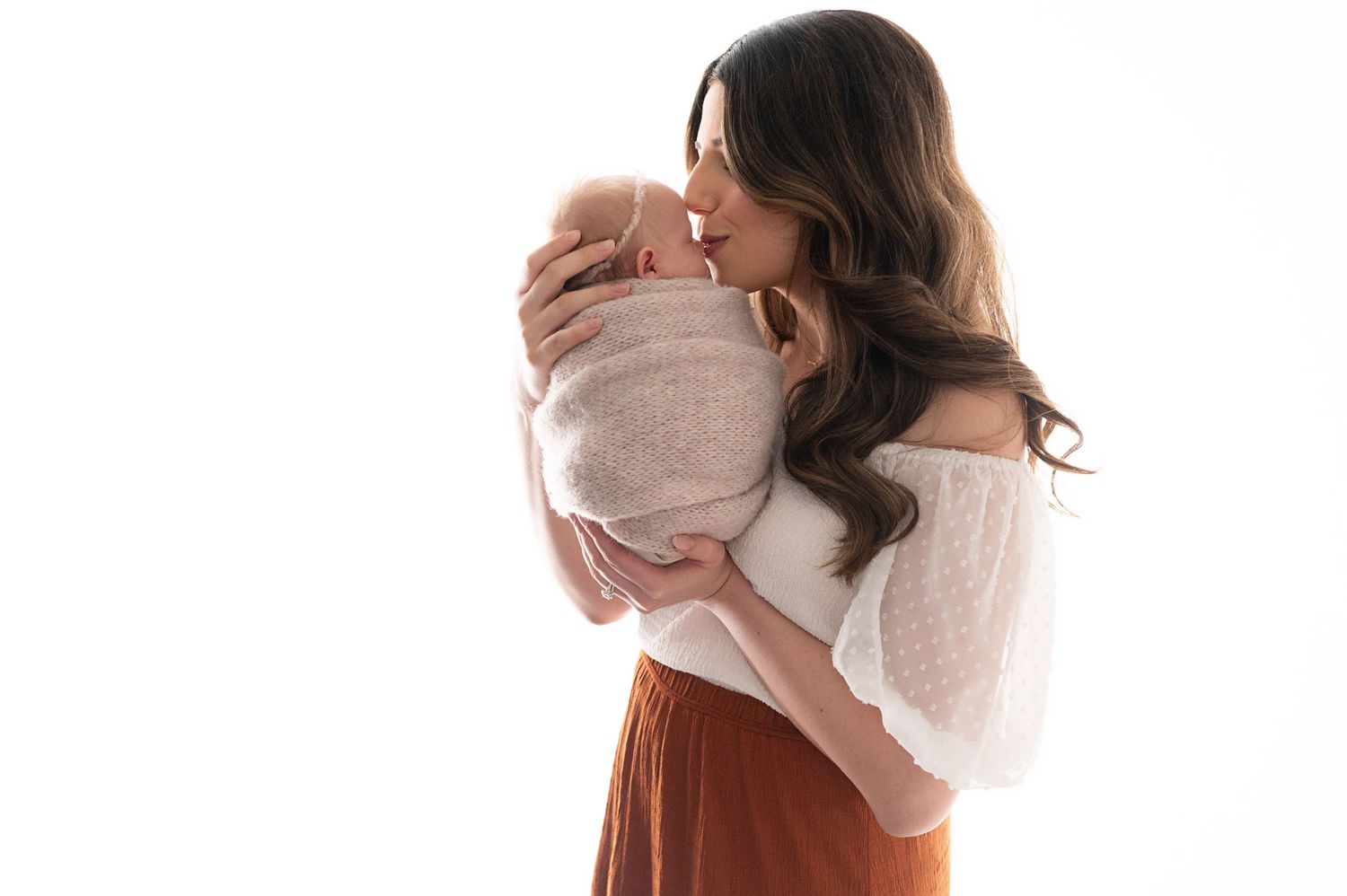 Parent in white top holding swaddled baby against neutral background.