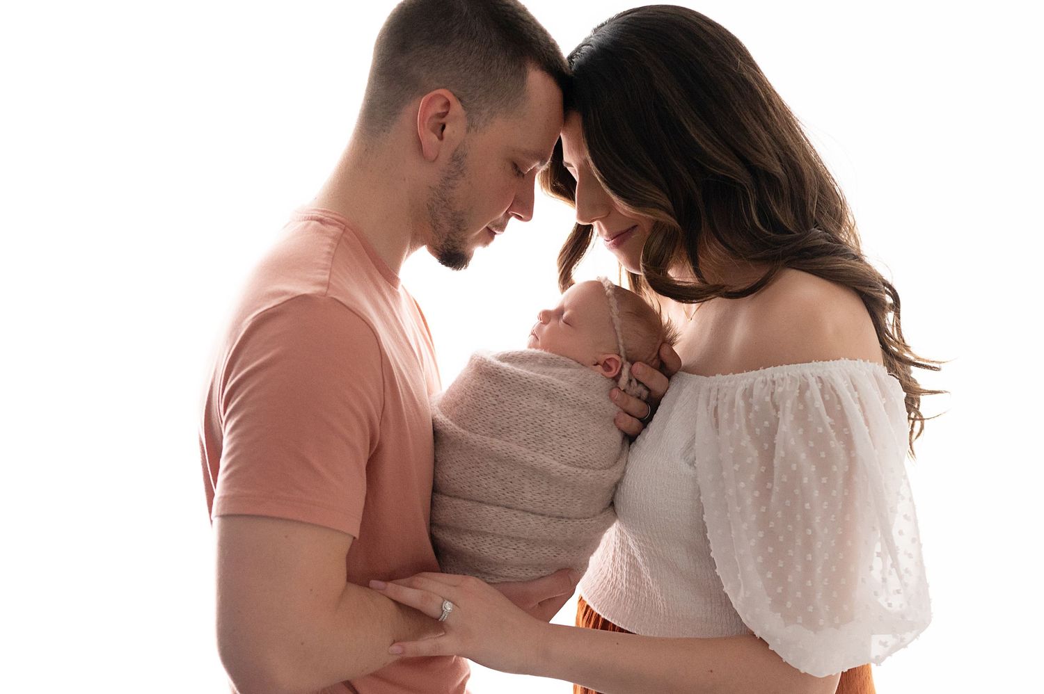 Intimate family moment with couple in casual attire holding their wrapped newborn.