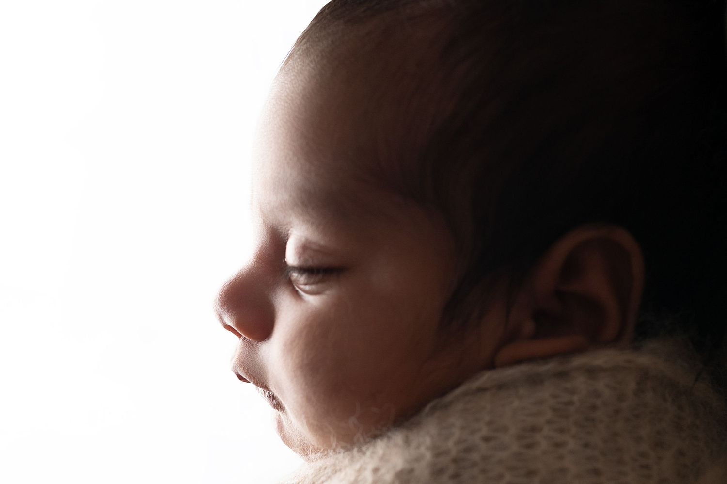 Close-up profile view of a baby's face against a dark background with dramatic lighting.