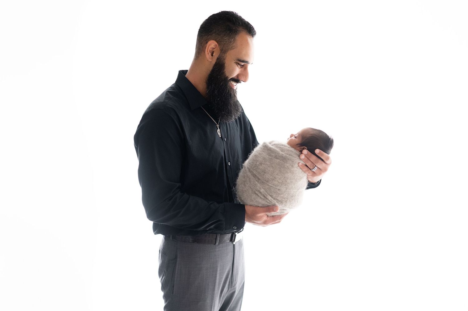 A person in dark clothing tenderly holds swaddled newborn against white background.