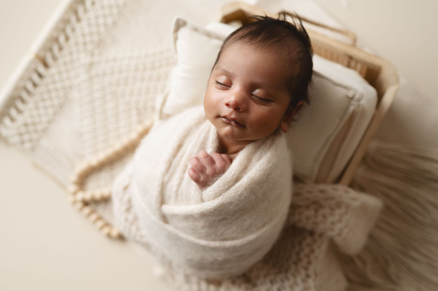 Sleeping newborn wrapped in white blanket rests on textured bedding.