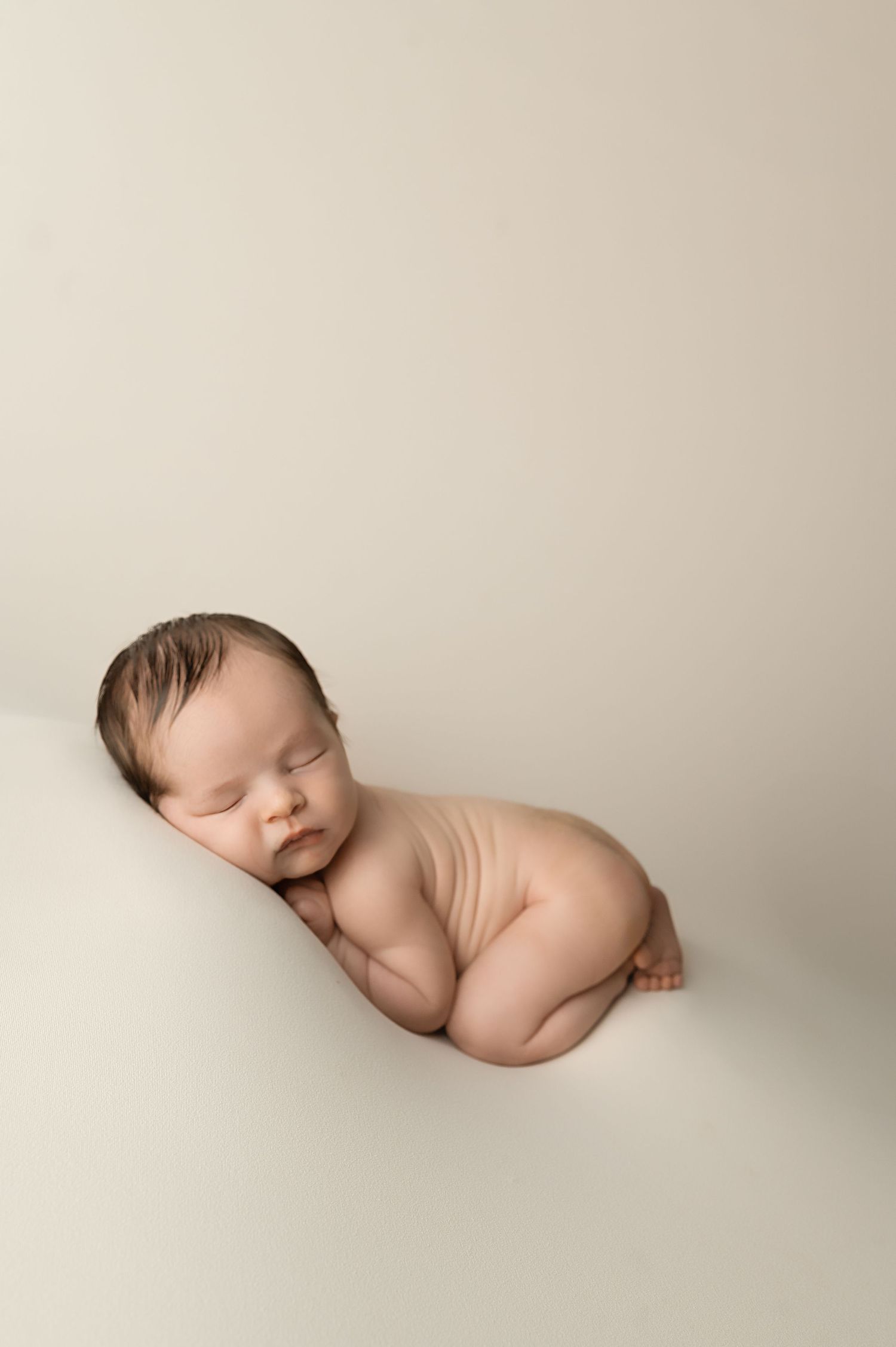 Artistic newborn photography photo shows peaceful sleeping baby in minimalist beige studio setting.