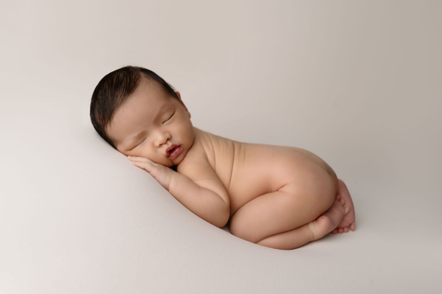 Sleeping newborn posed on side without wrapping on neutral backdrop.