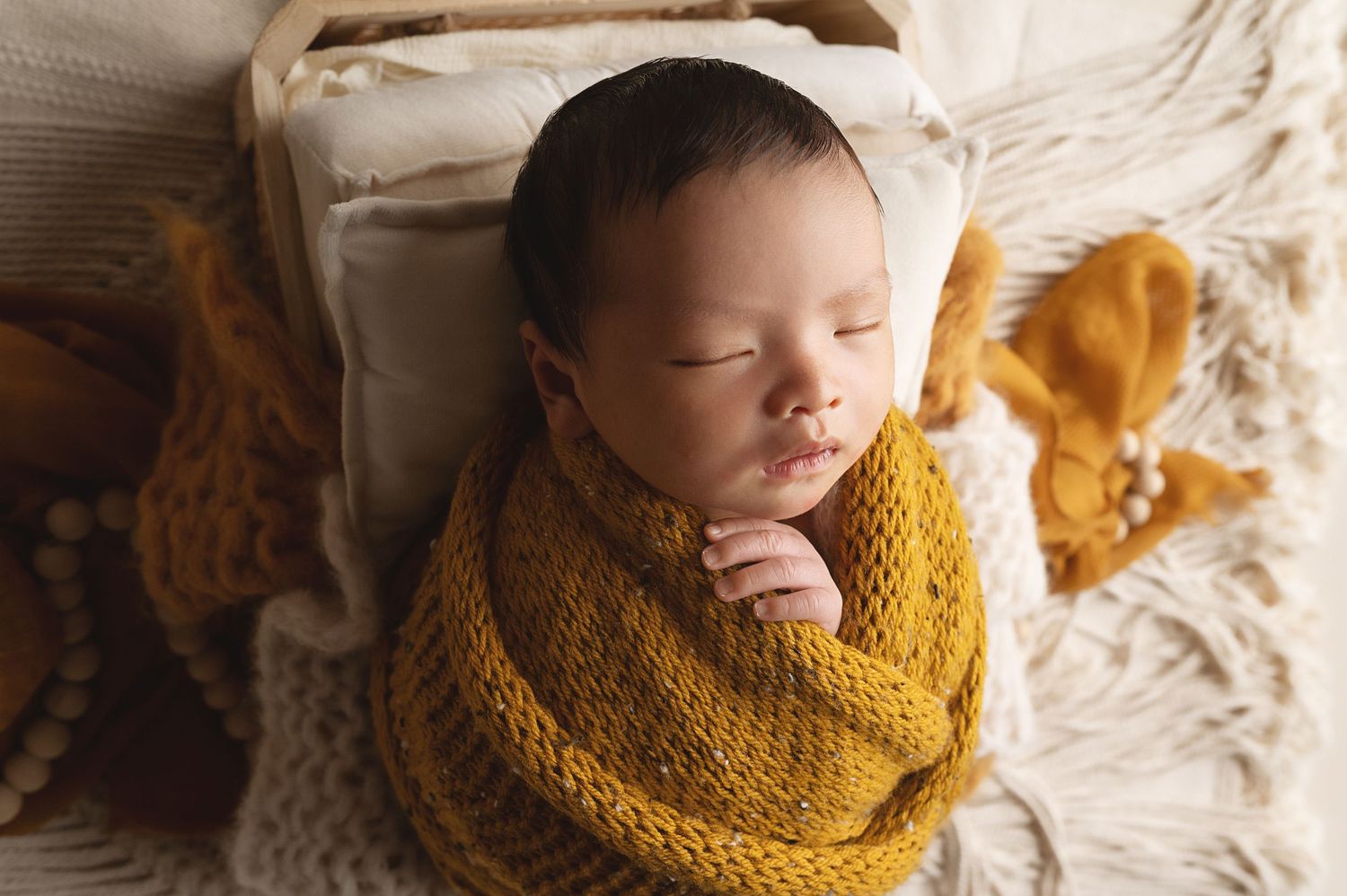 Peaceful sleeping newborn wrapped in cozy yellow knit blanket during professional photoshoot.