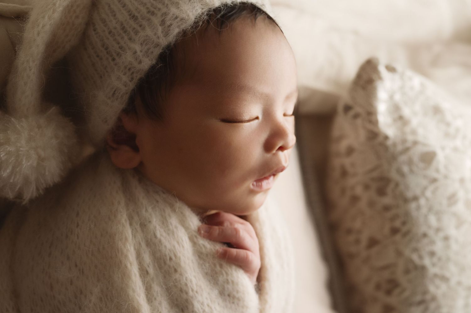 Peaceful newborn sleeping while wrapped in soft cream knit blanket.