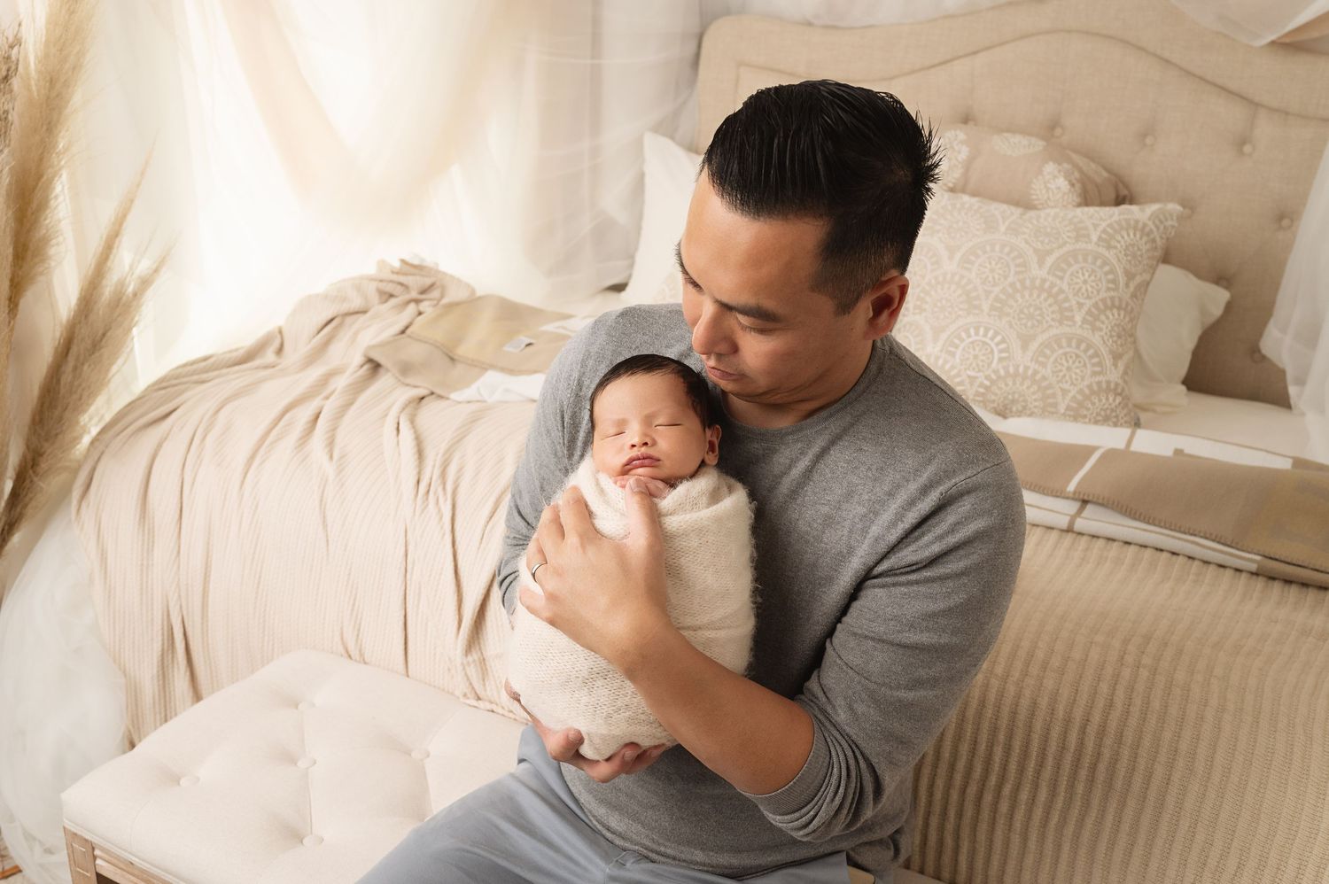 Tender moment between parent and swaddled newborn baby on cream colored bedding.