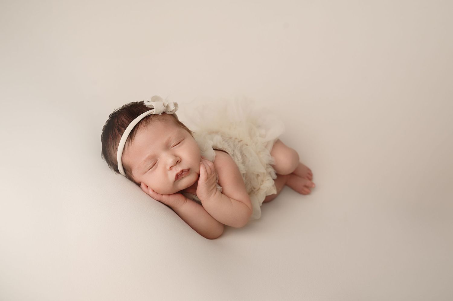 Sleeping newborn wearing lace outfit and headband during professional photography session.