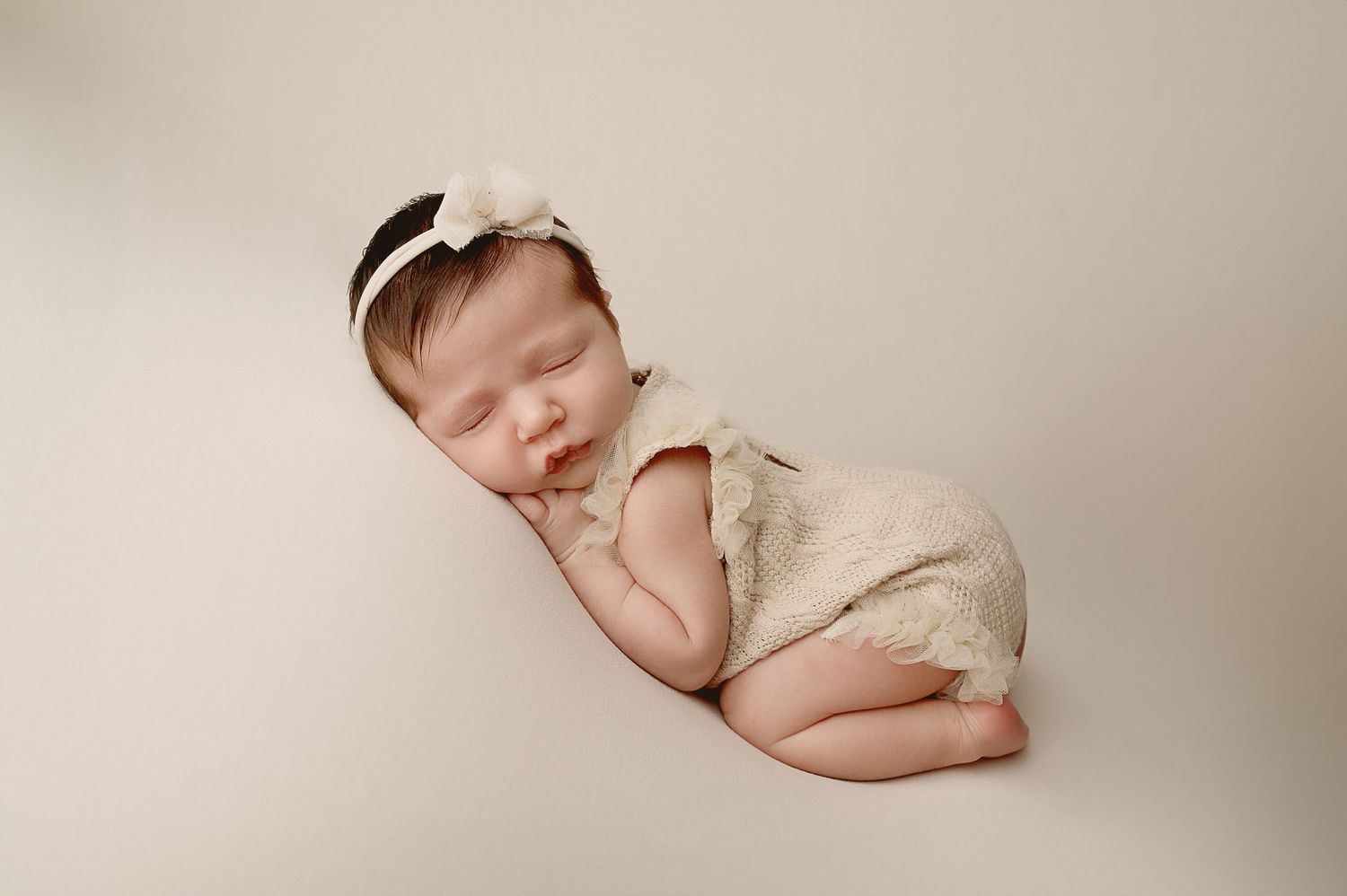 Side view of sleeping newborn in cream outfit during studio photography session.