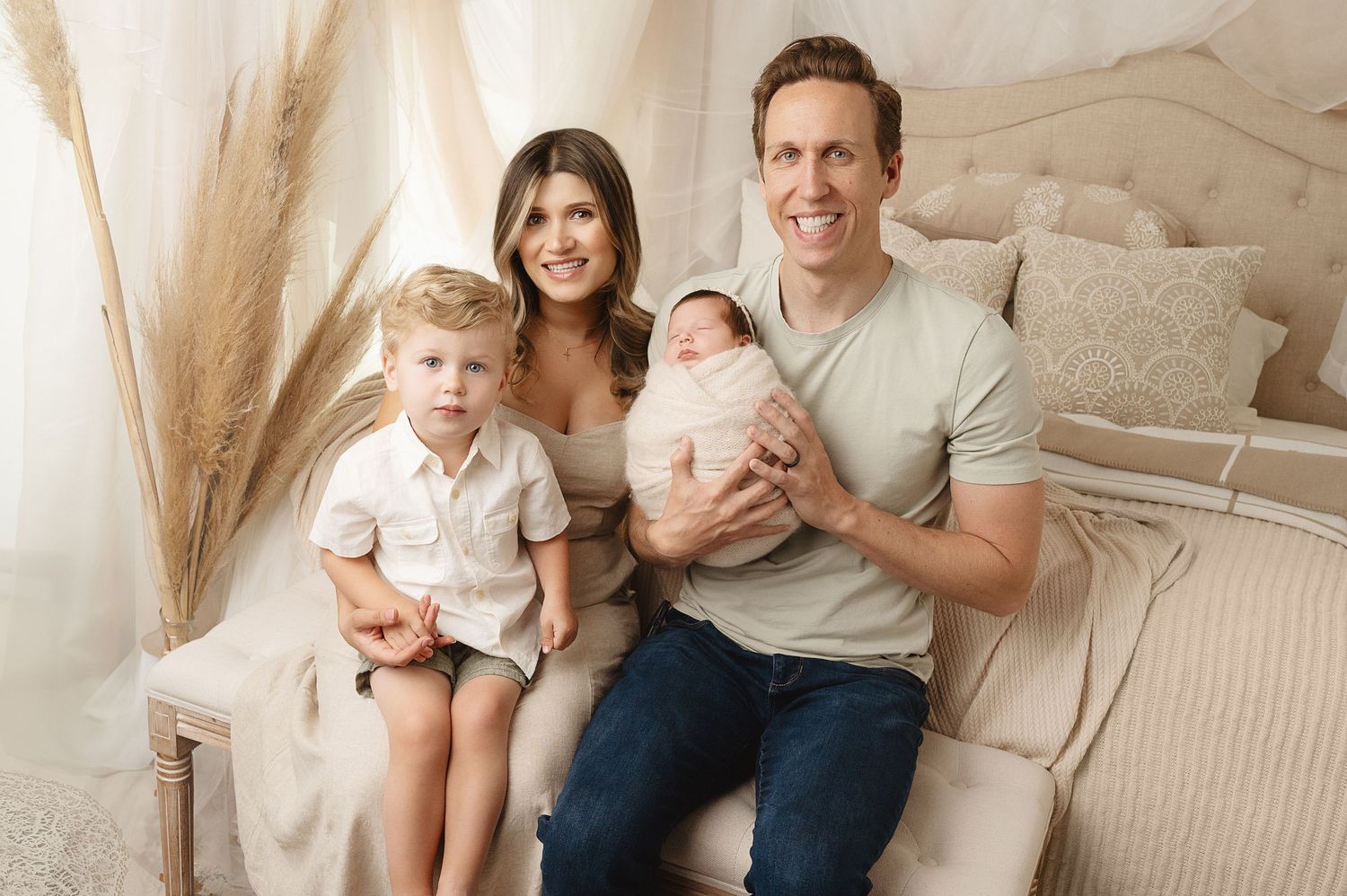 Modern family studio portrait with toddler and newborn on neutral backdrop.