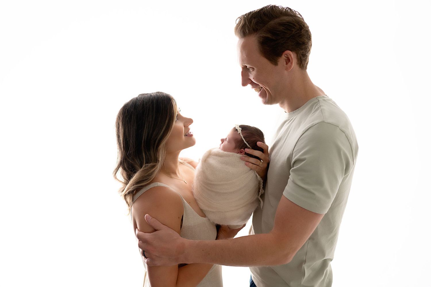 Parents holding their newborn baby together in a tender embrace against white background.