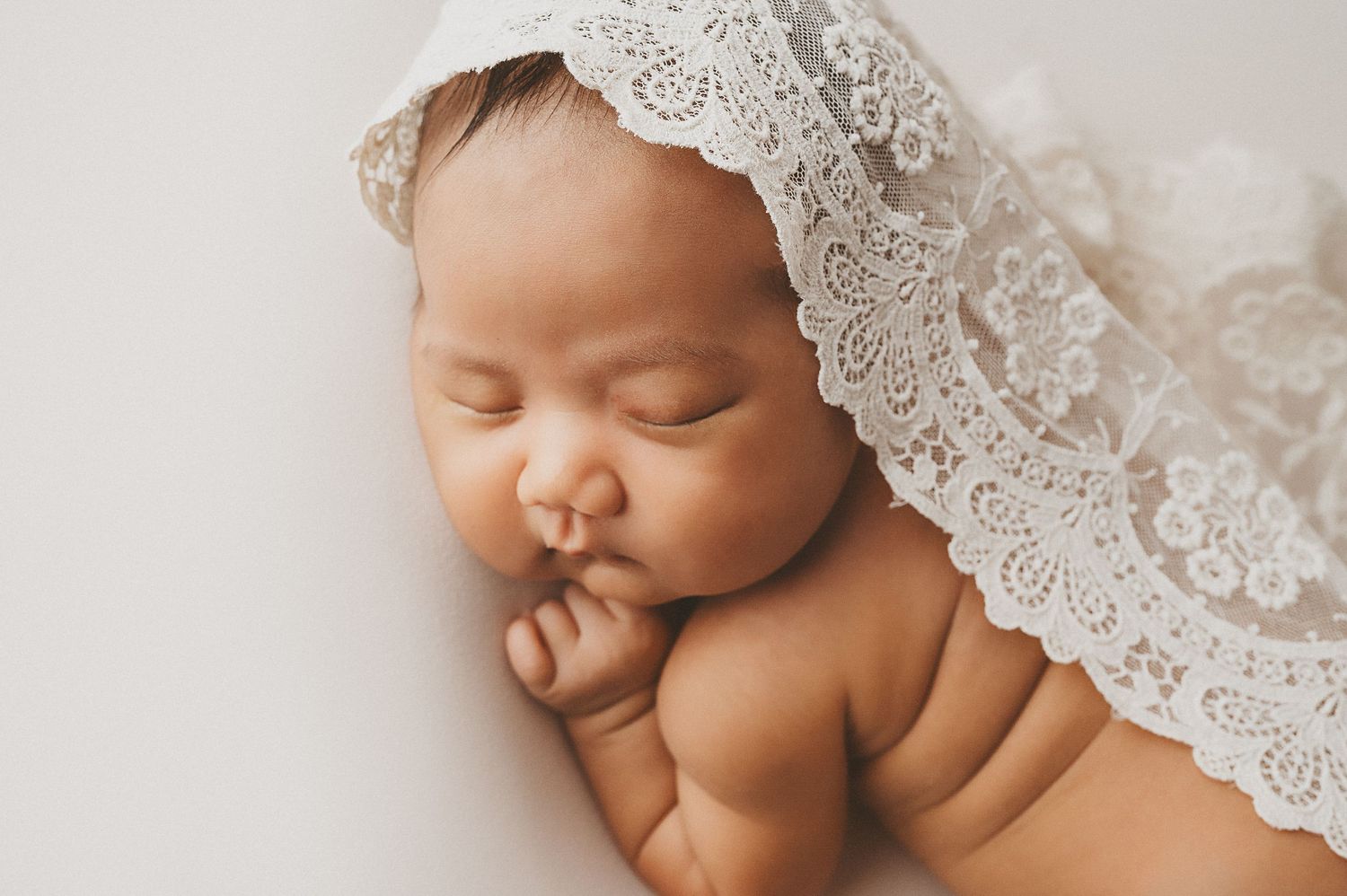 Sleeping newborn baby with delicate lace covering in soft natural light.