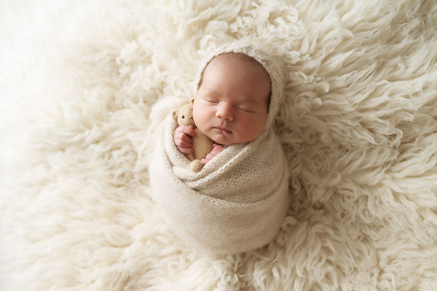 Sleeping newborn wrapped in cozy cream blanket on fluffy white carpet.