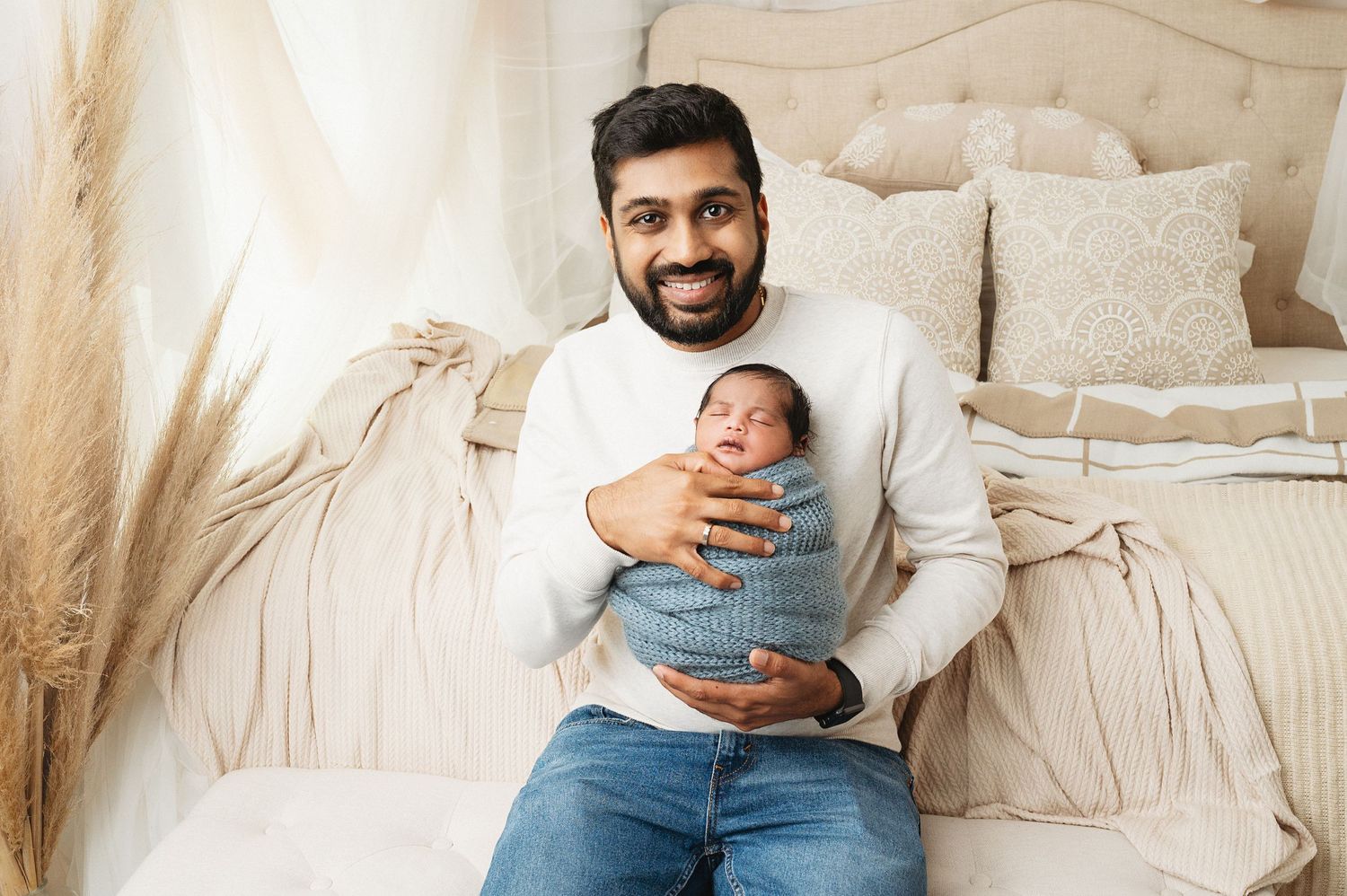 Parent sitting on bed cradles newborn baby in casual home setting.