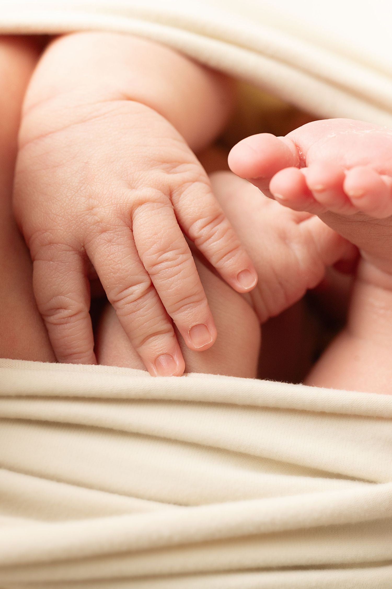 Delicate baby hand and fingers resting on soft beige fabric.