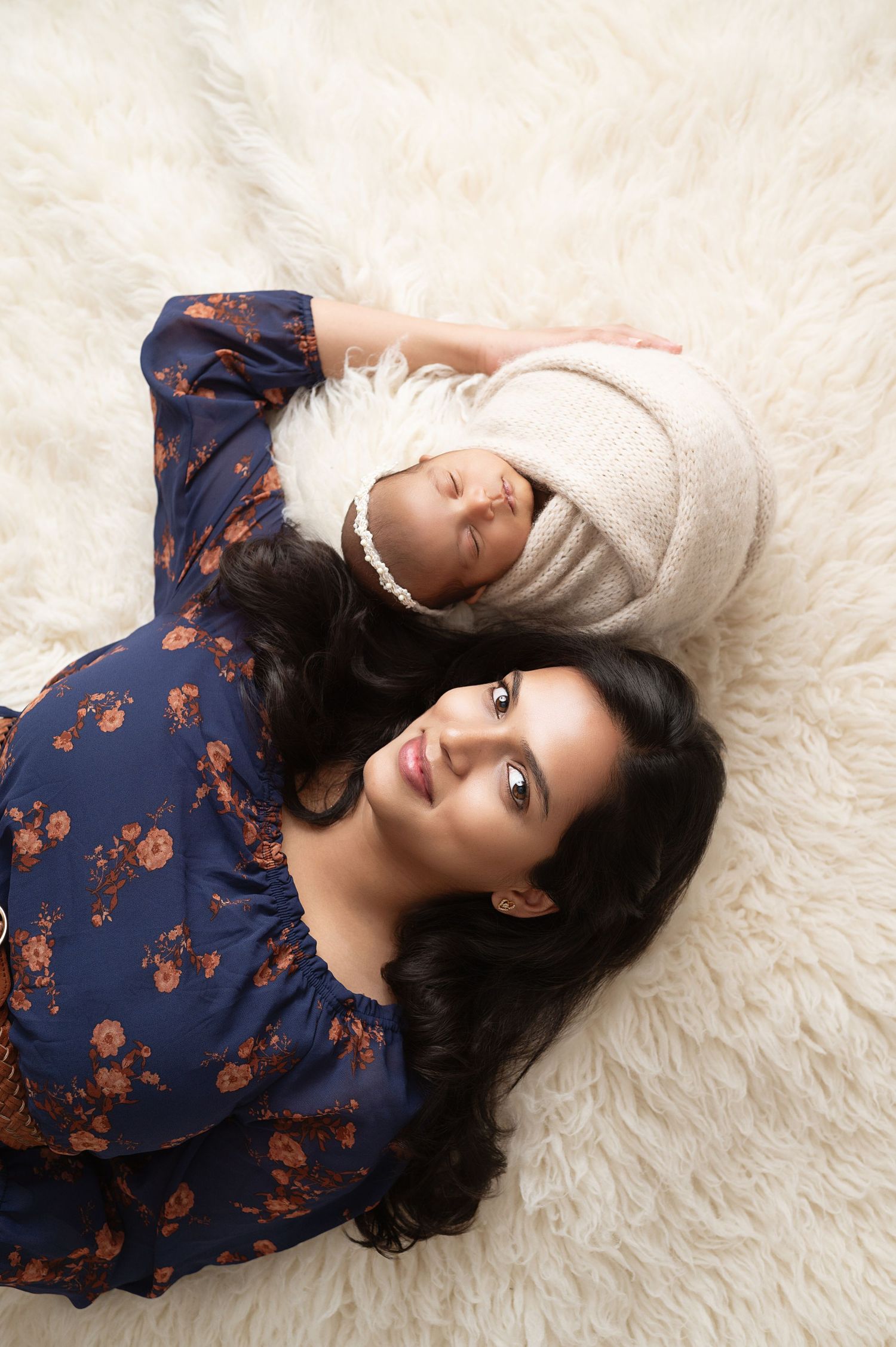Woman in floral dress laying on plush white rug during maternity session.