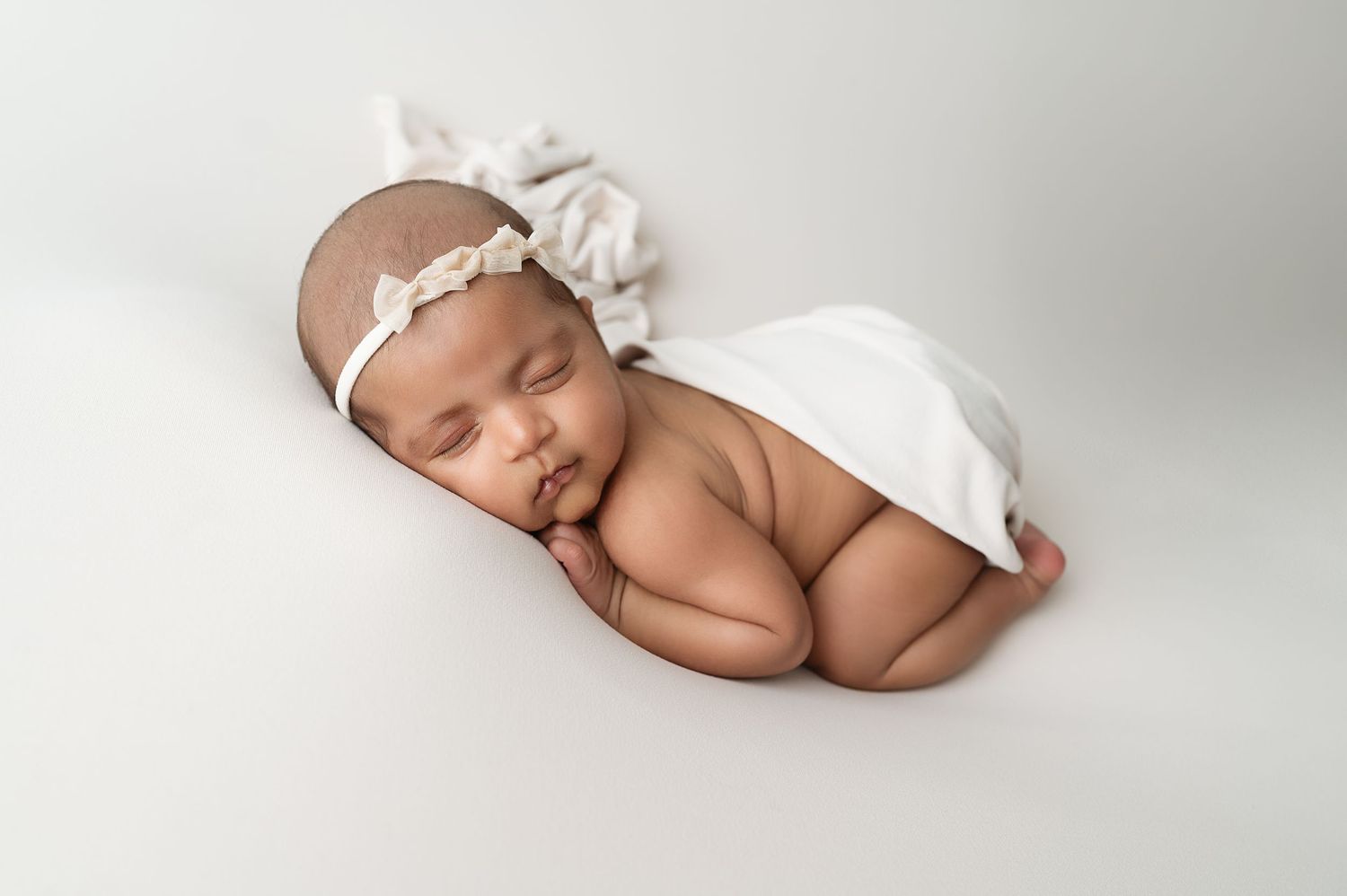 A peaceful newborn baby sleeping on a white backdrop in minimalist photography style.