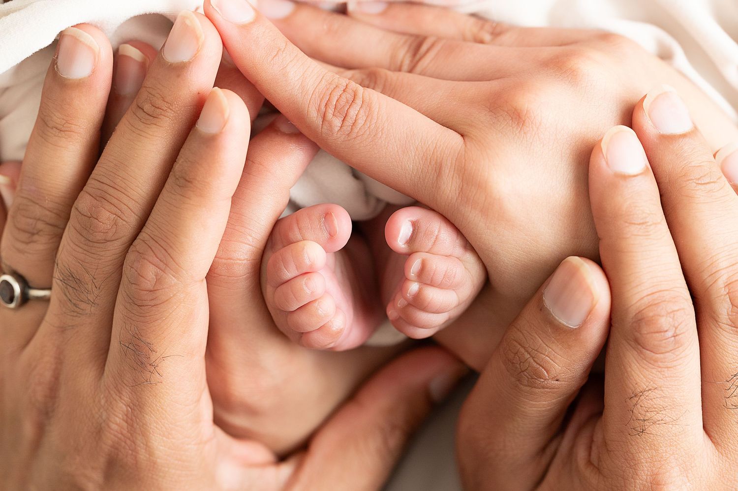 Close-up shots of tiny newborn fingers and hands being gently held against white background.