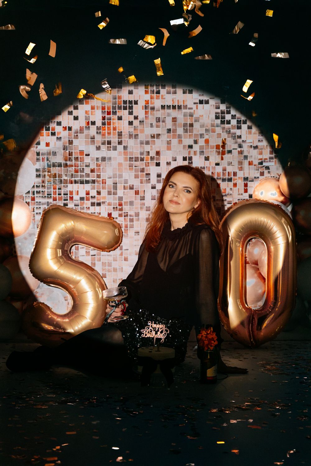 Birthday celebration setup with gold number 50 balloons against sparkly backdrop with falling confetti.