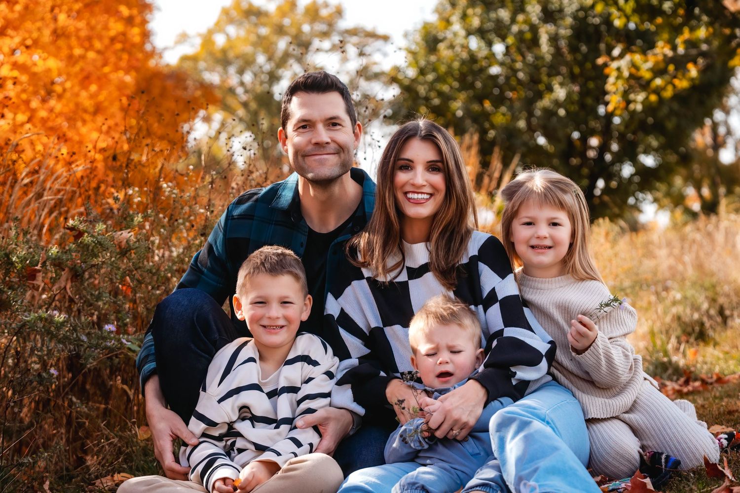 Family portrait by water with children, mother in red dress and father in olive shirt.
