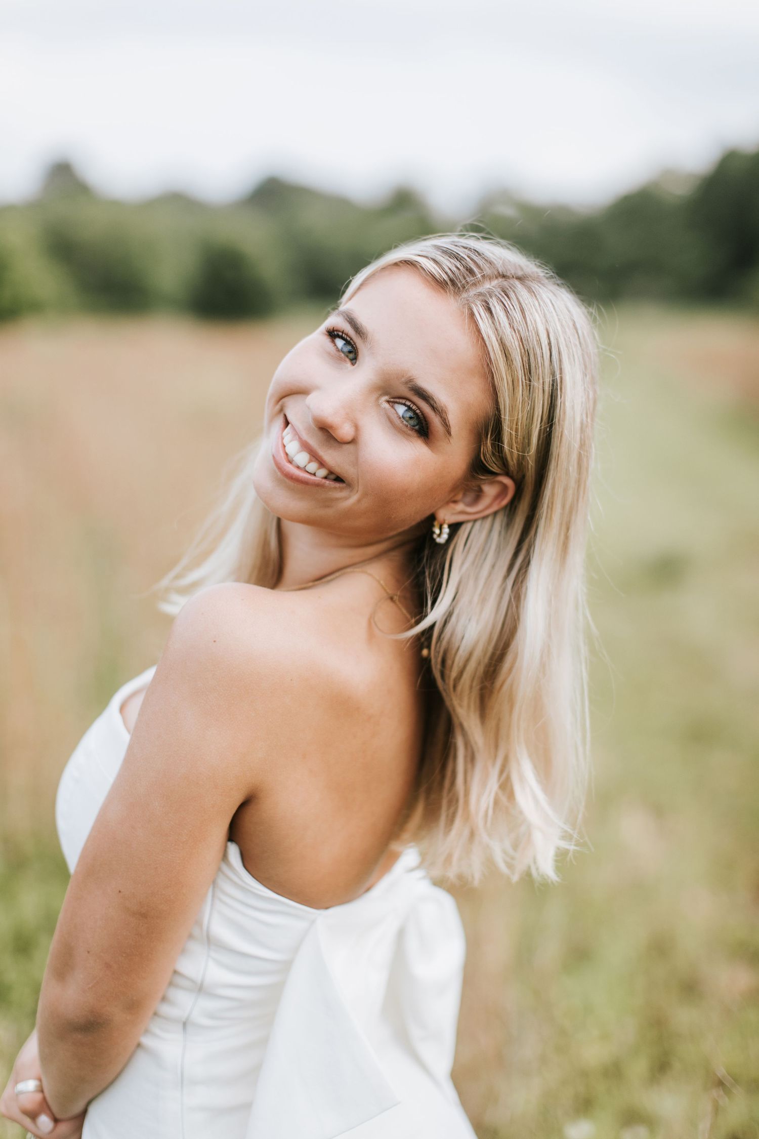 A joyful moment captured in a field as someone in a white dress smiles over their shoulder on a sunny day.
