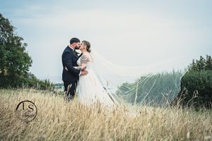A couple shares a romantic moment in a golden wheat field with mountains and trees in the background.