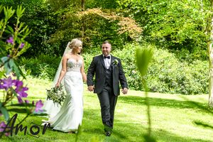 Couple walking together on a sunny garden path surrounded by lush greenery and colorful flowers.