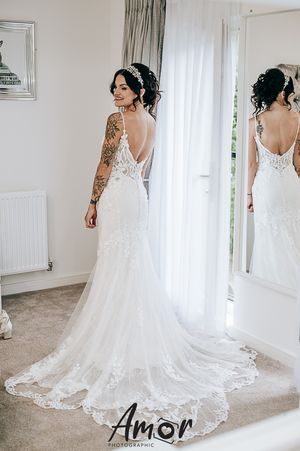 Back view of an elegant lace wedding dress with open back design and flowing train in a bright dressing room.
