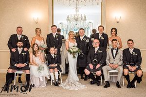 Elegant formal wedding party in black and white attire posed together in luxurious room with crystal chandelier.