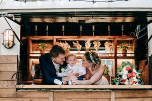 Wedding reception guests enjoy drinks and conversation at a wooden bar counter in an intimate indoor setting.