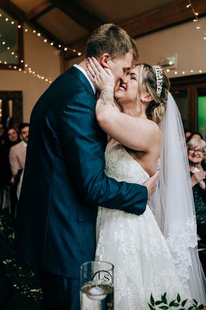 A romantic moment between newlyweds sharing their first kiss at a wedding reception with string lights and decor.