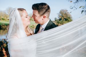 A flowing white veil blows in the wind as a couple shares a romantic moment outdoors on their wedding day.