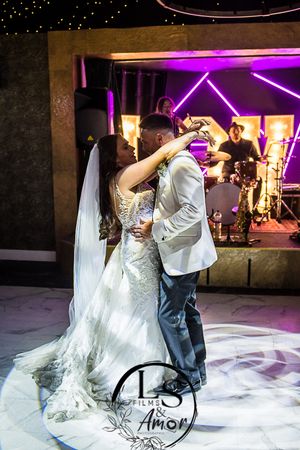A couple dances together on a white illuminated dance floor under purple lights at an elegant wedding reception.