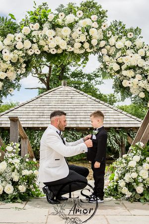 Beautiful white floral wedding arch frames a touching moment under cloudy skies at an outdoor venue.