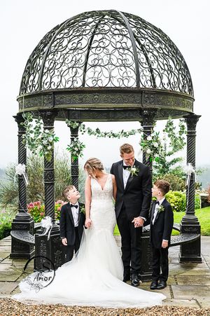 Elegant wedding party standing under ornate black metal gazebo with domed roof and floral decorations at outdoor venue.