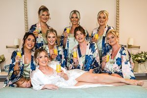 Group in matching floral robes posing together before a wedding celebration with mimosa drinks.