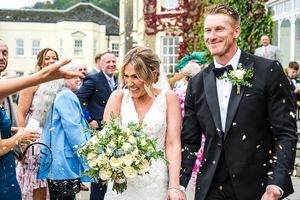 Wedding guests shower the happy couple with confetti as they exit their ceremony holding a beautiful white flower bouquet.