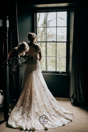 Elegant lace wedding dress displayed near a sunlit window in a dark rustic room, shown from multiple angles.
