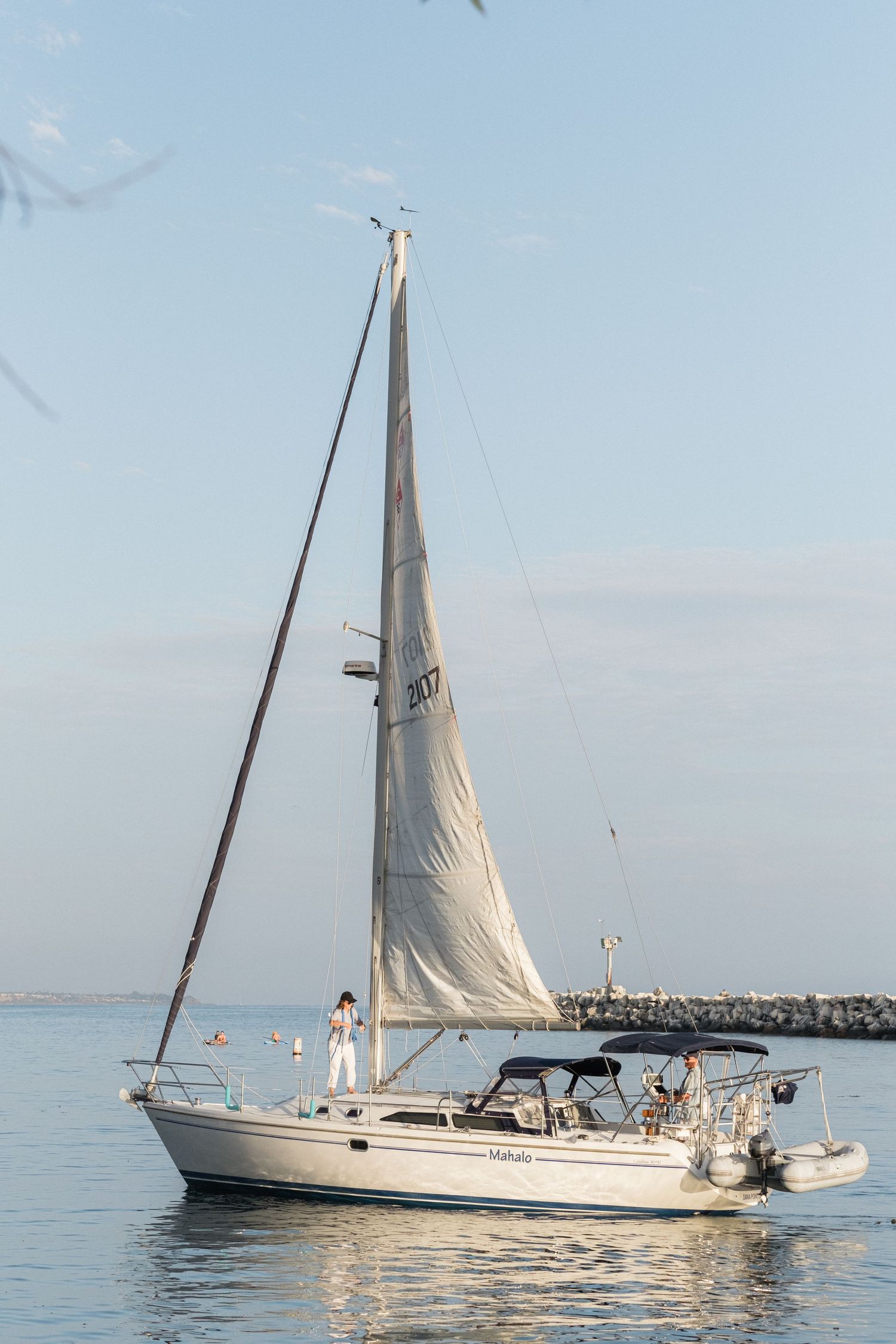 White sailboat gliding across calm waters with clear blue sky in the background.