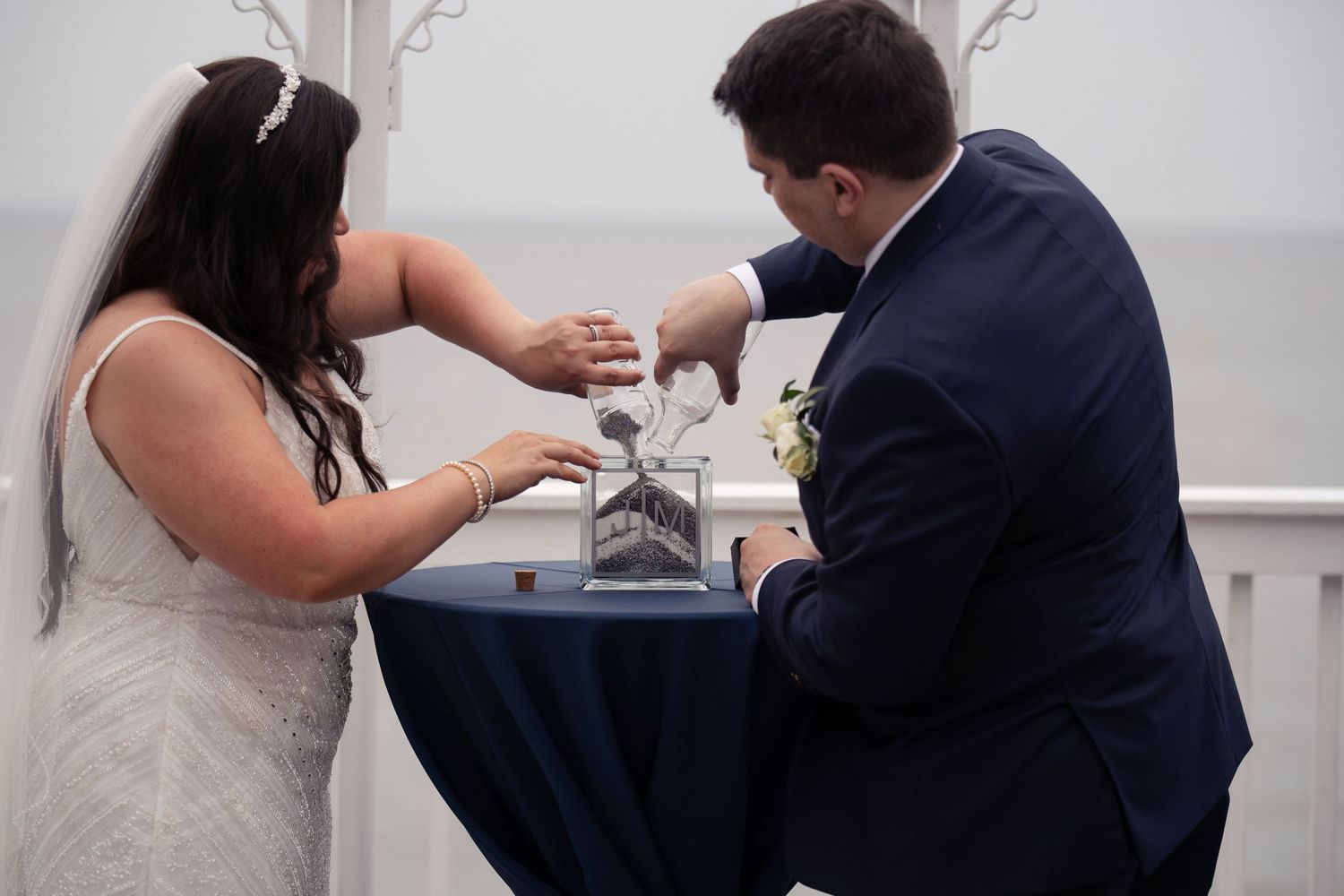 Wedding couple participates in a unity ceremony at a small blue table during their reception.