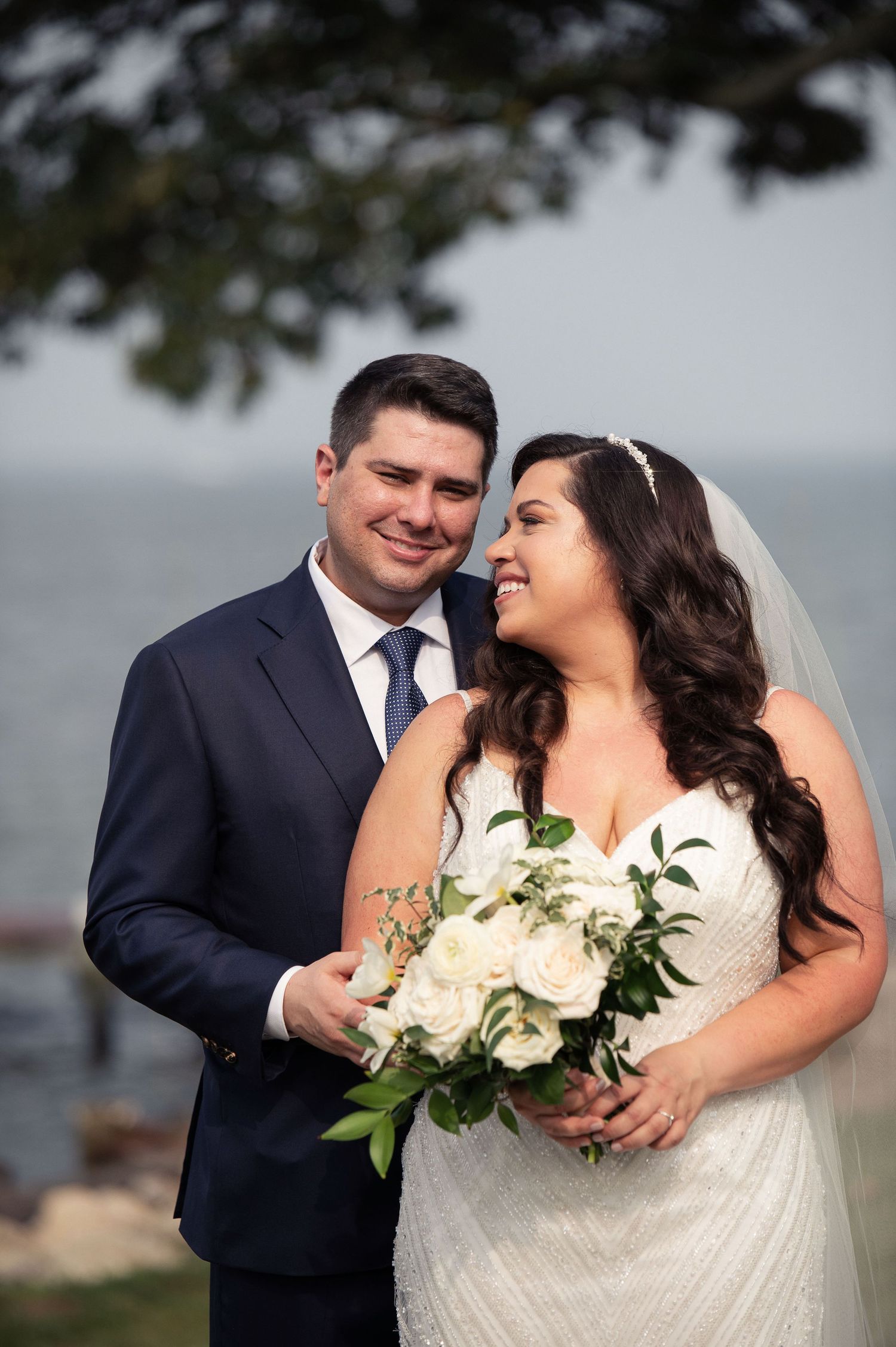 Wedding portrait with white rose bouquet against ocean backdrop.