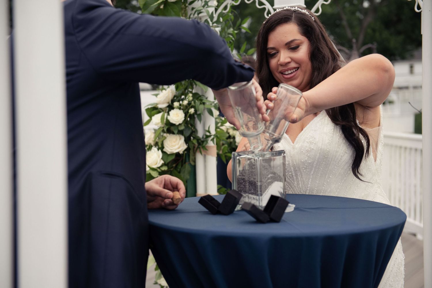 Newlyweds perform unity ceremony pouring sand at blue-draped table.